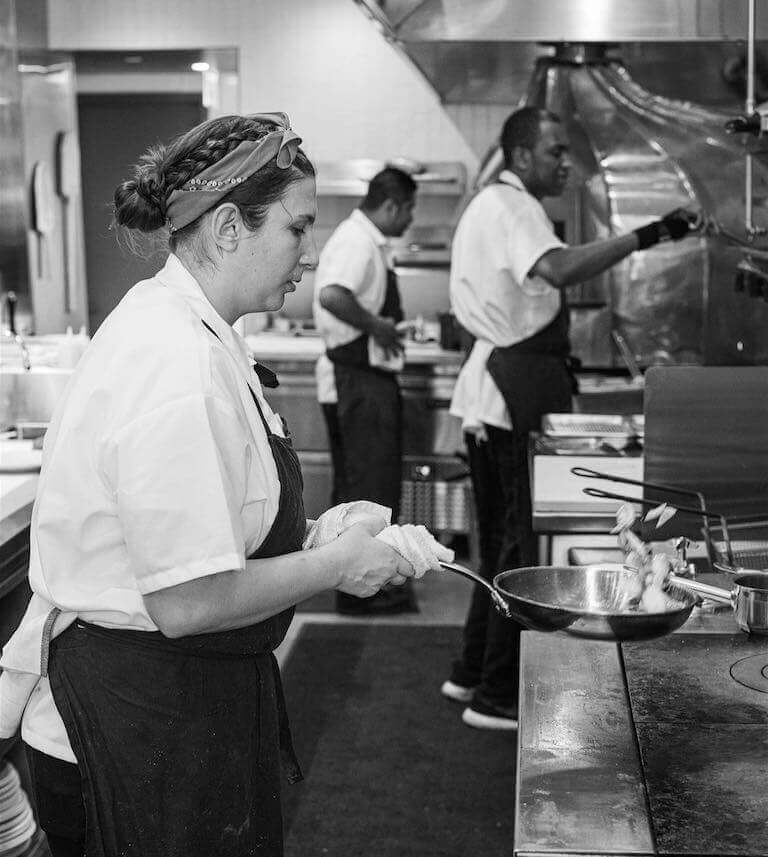 Chef Maggie cooking with a pan in a restaurant kitchen