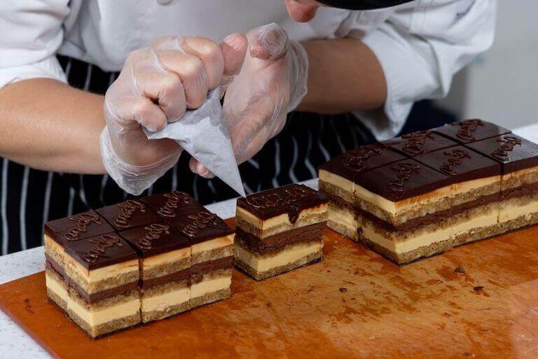 Chef piping chocolate details on opera cake
