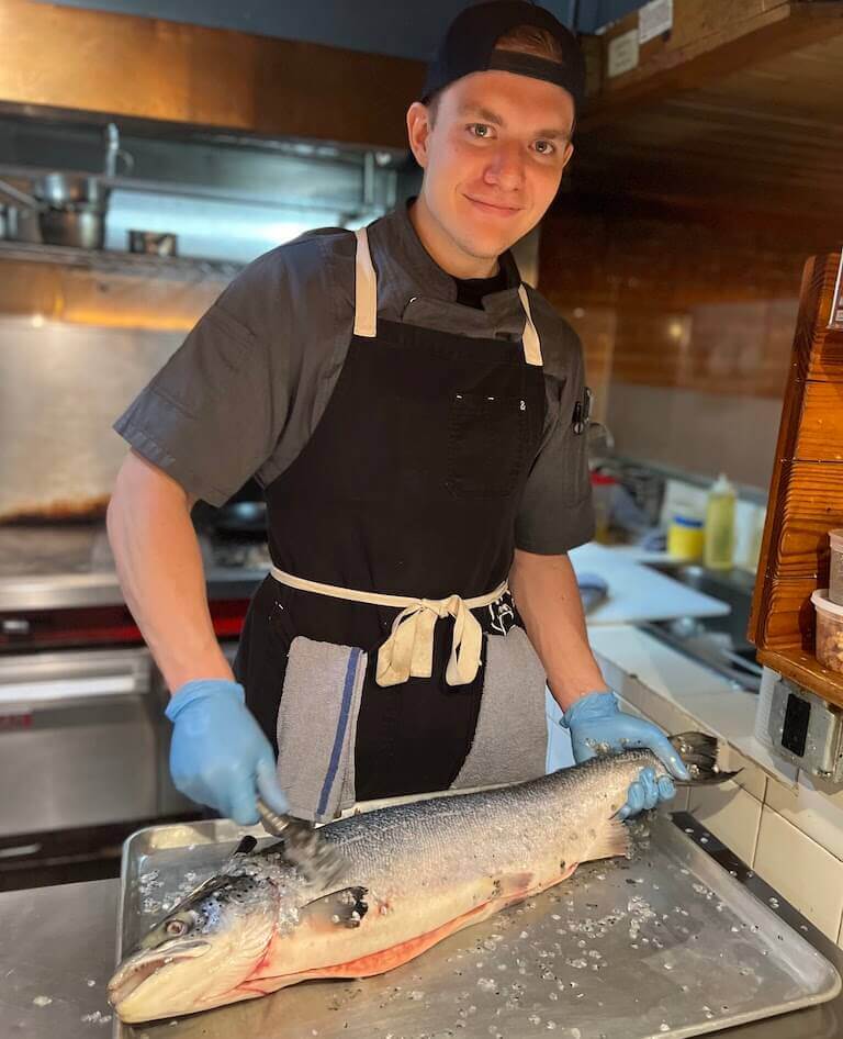Jackson descaling a salmon in the kitchen at La Marmotte