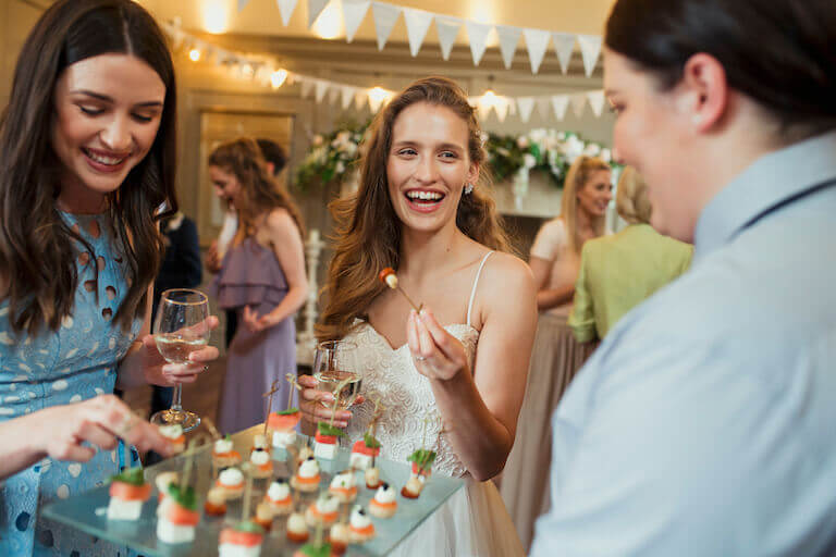 A server offers a tray of passed appetizers to two smiling female party guests