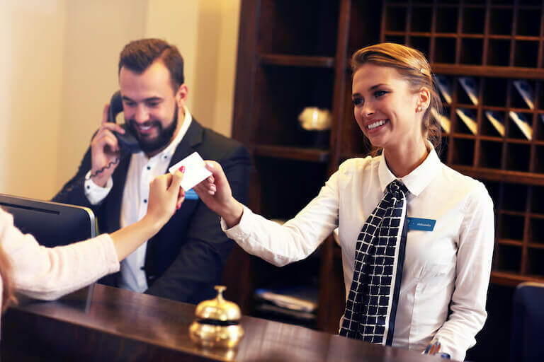 A smiling female hotel clerk takes a credit card from a customer.