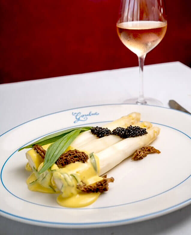 white asparagus with sauce on a white plate with a glass of wine