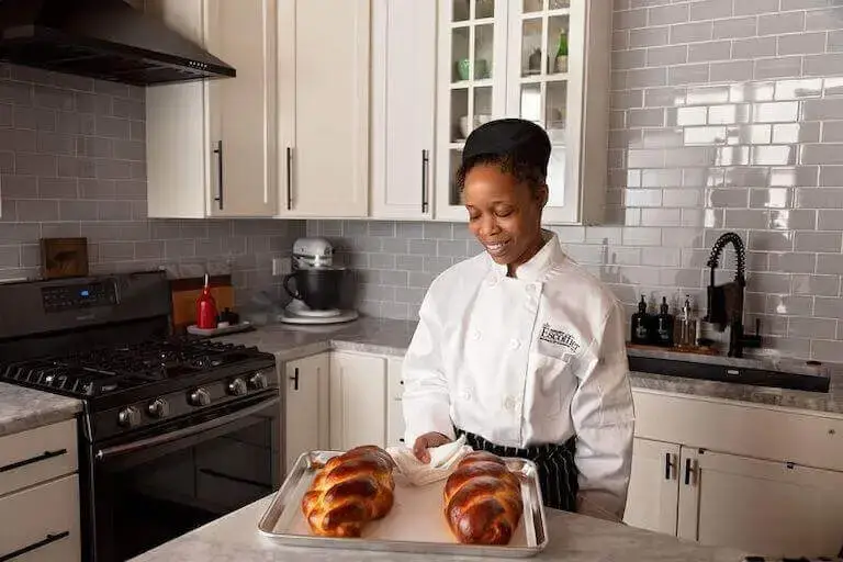 Escoffier online student smiling and holding a baking sheet with finished bread.