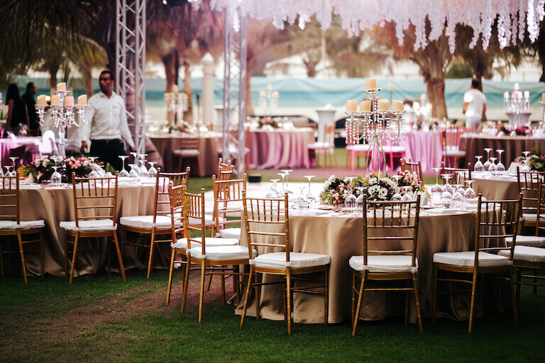 Servers make last-minute adjustments to large tables decked out with ornate candelabras, flower arrangements, and fancy place settings.