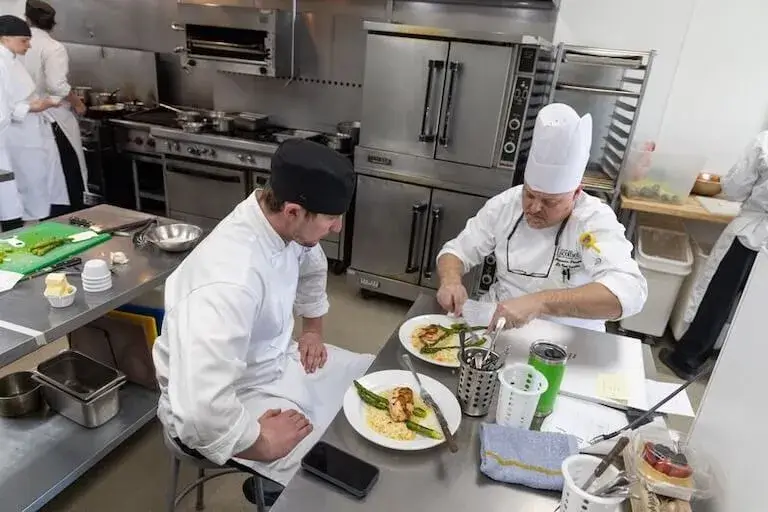 Chef Instructor and student reviewing prepared dishes during hands-on culinary training