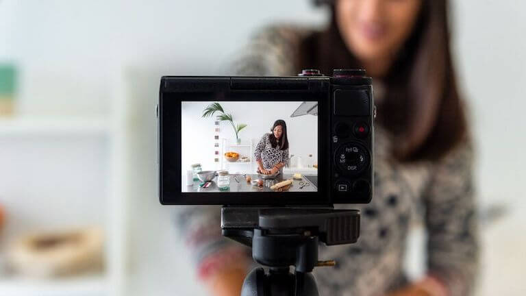 A close-up view of the screen on a digital camera, showing a woman doing a cooking demo at a kitchen island.