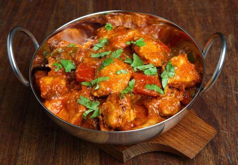 A stainless steel bowl with chicken tikka jalfrezi curry sitting on a wooden table.