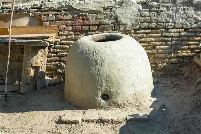 An domed Uzbeki tandoor oven stands before a hand-laid brick wall in an bright, arid climate.