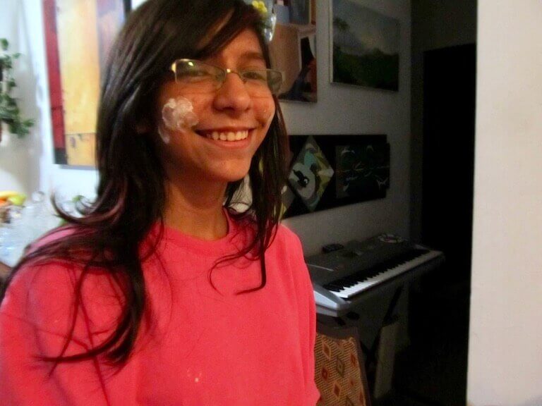 A closeup photo of Estefania Colamarco at about 13 years old. She wears glasses and is smiling, and she has powdered sugar on her cheek.