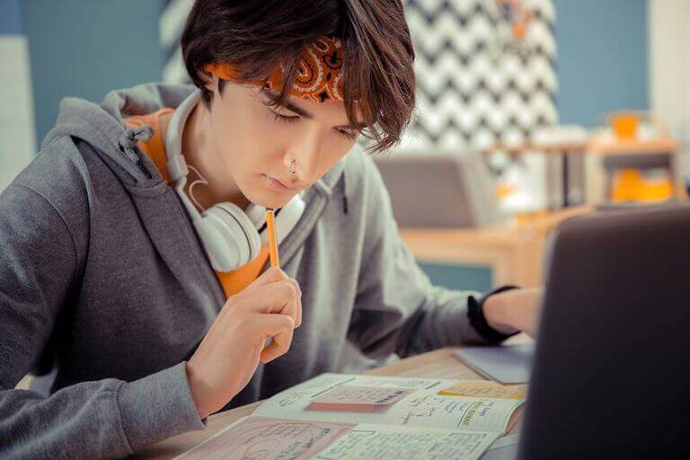 An engaged student sitting down in a classroom environment, studying with a textbook and laptop open.