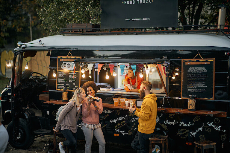 Food truck trailer with three people eating their food while the server looks on smiling.