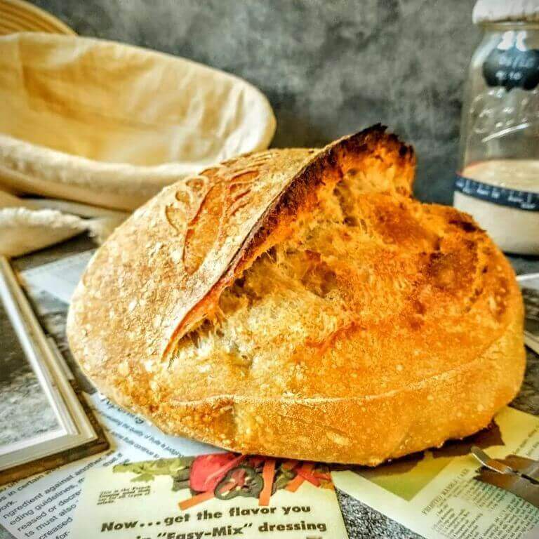 A round loaf of sourdough bread with a large ear scored down its front.