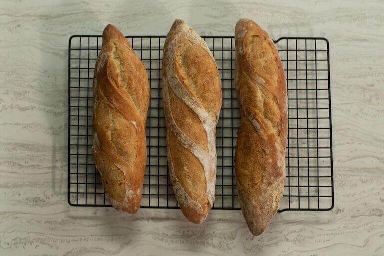 An overhead view looking down at the tops of three baguettes sitting on a cooling rack.