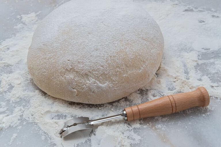 Freshly risen classic French boule bread dough on a marble pastry board with a lame, getting ready for scoring.