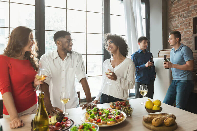 A group of people in upscale casual attire smile and laugh as they drink beer and wine and enjoy hors d'oeuvres in a bright, airy event space.