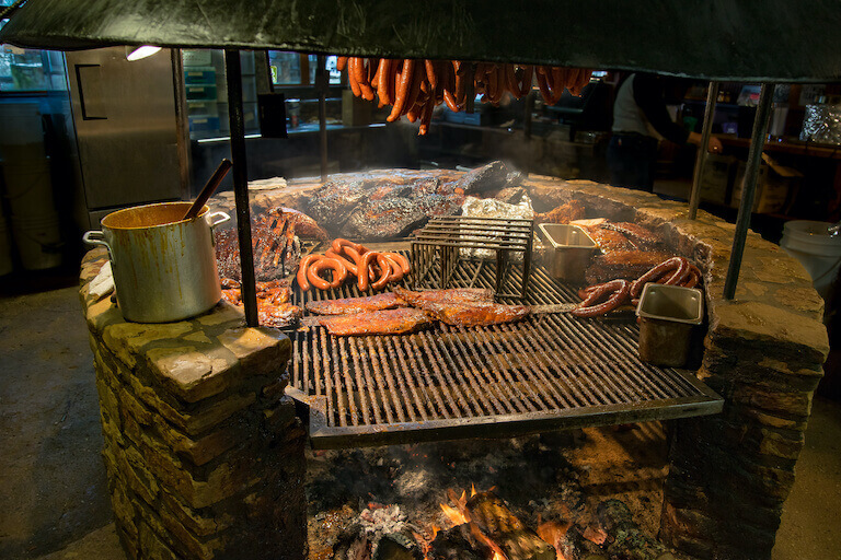 A large grill cooking various cuts of meat and linked sausages.