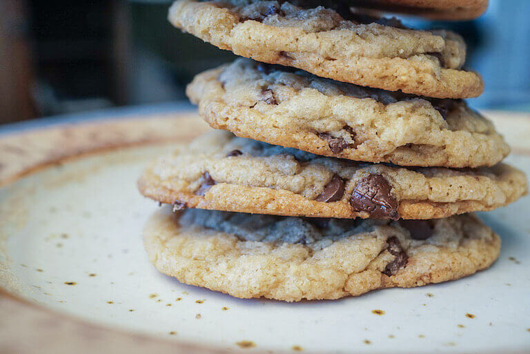 A plate stacked with four chocolate chip cookies. 