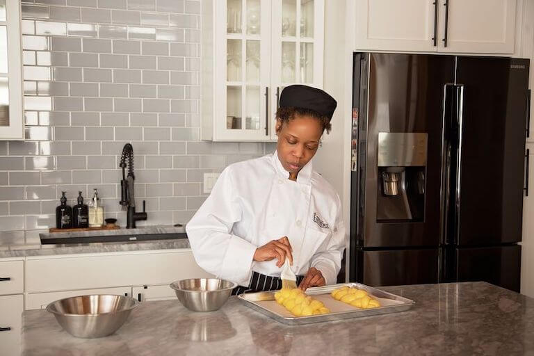 Pastry chef standing in a home kitchen at counter brushing egg wash on challah dough.