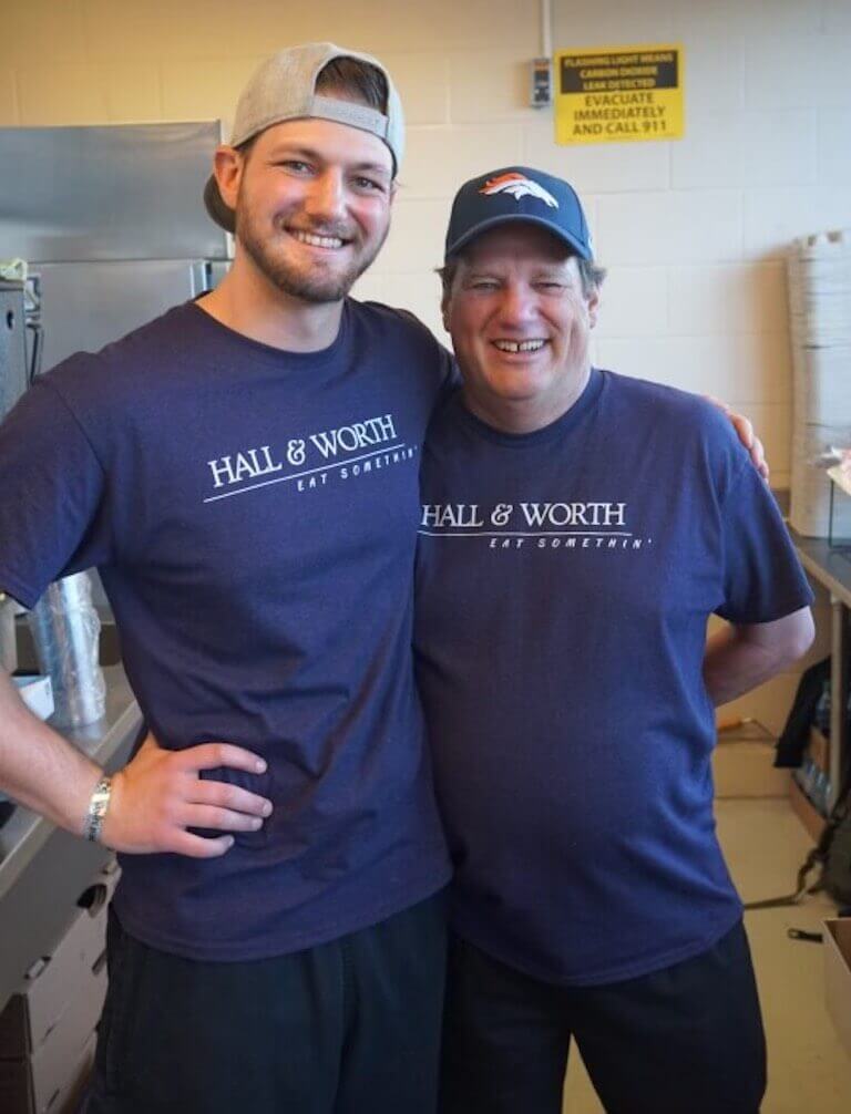 Wes Duckworth and a business associate donning navy blue Hall & Worth t-shirts and smiling in a stadium kitchen.