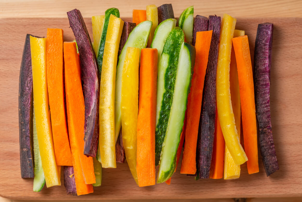 top view of colorful carrots and cucumbers vegetables julienned on wooden board
