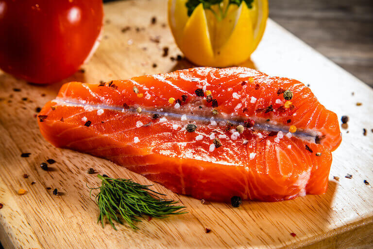 A piece of salmon is shown with a butterfly cut and spices sprinkled on each side.