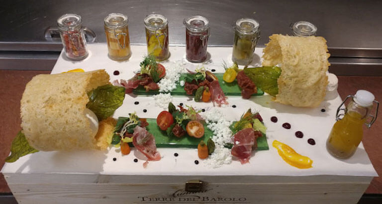 An elaborately plated antipasto platter featuring basil gelee, Iberico ham, olive oil powder, 100-year balsamic, house burrata, parmesan crisp, and assorted pickles.