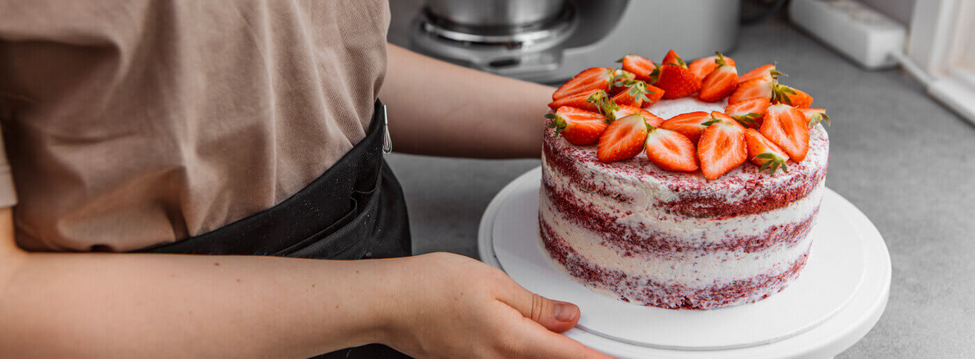 Close up of red velvet cake topped with strawberries held by a pastry chef