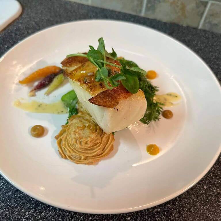 Cooked sea bass on a white plate with an herb garnish.