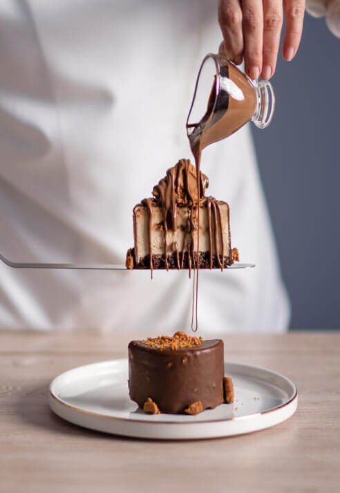 Female chef pouring chocolate sauce on a cake slice