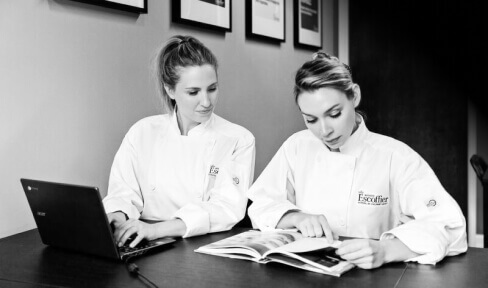 Two Escoffier students looking at a recipe book