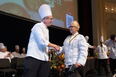 Escoffier Boulder Chef Instructor shaking a hand with an Escoffier graduate at the Graduation 2022 ceremony