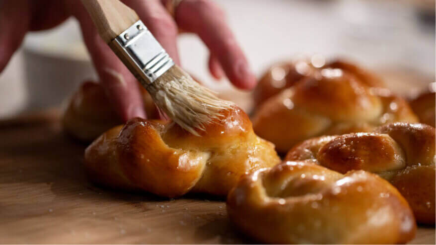 A baker spreads butter on fresh pretzels