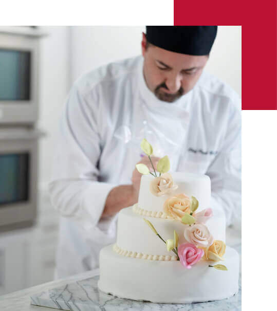 An Escoffier baking and pastry arts chef instructor puts the finishing touches on a white wedding cake with flowers