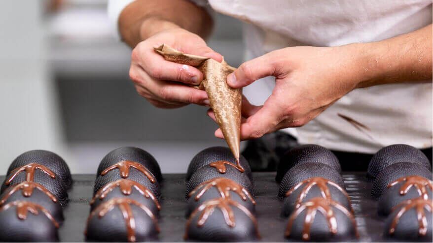 A pastry arts student pipes chocolate topping onto chocolate truffles