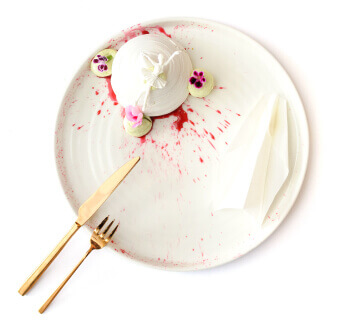 A gourmet white meringue dessert with berry sauce and flowers on a white plate