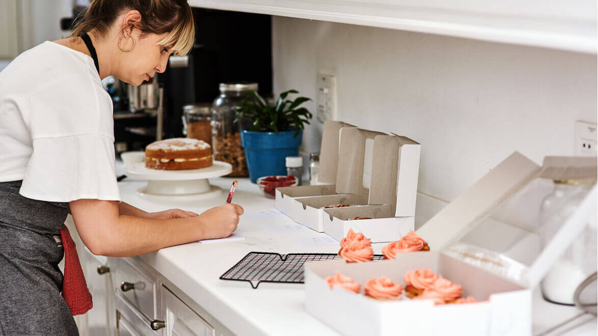 A home baker packs cupcakes in pastry boxes in her home kitchen