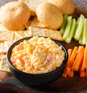 Pimento cheese dip in a bowl with bread, crackers, carrots and celery.