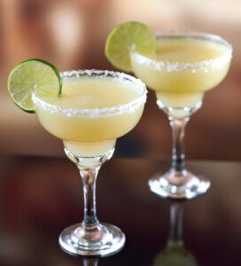 Two lime margaritas in stemmed glasses rimmed with salt and garnished with lime wheels.