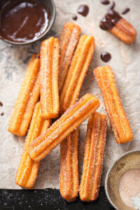 Churros stacked on paper with a bowl of chocolate dip.