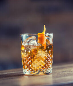 Old Fashioned cocktail in crystal rocks glass with ice and orange peel.