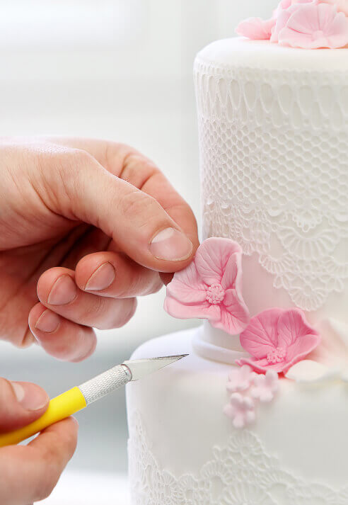 Male hands placing a pink sugar flower on a white wedding cake