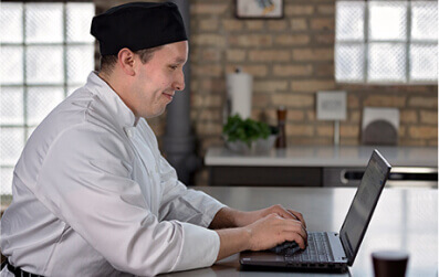 Escoffier online culinary student works on his laptop at his home