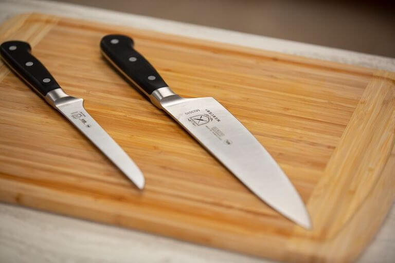A carving knife and a boning knife on a wooden cutting board. 