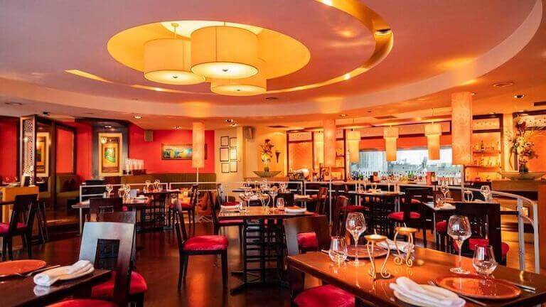 The dining room of a fine dining restaurant, featuring a variety of lighting fixture styles on the ceiling, at the bar, and on the tables.