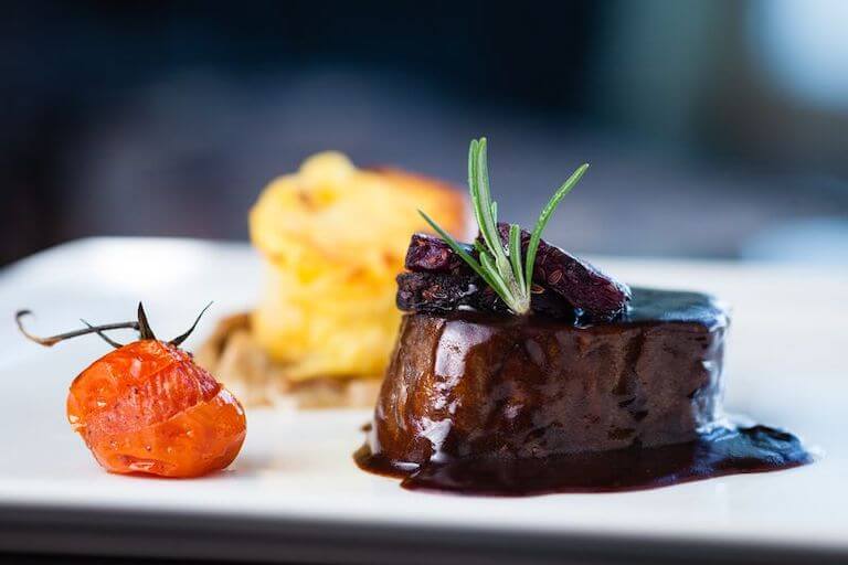 A cooked tenderloin roast, shown with rosemary and a roasted tomato.