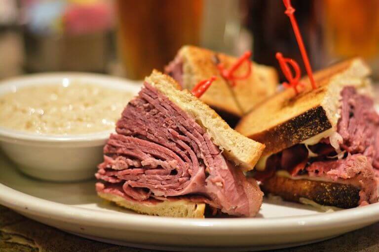 A corned beef sandwich on a plate next to a small cup of soup.
