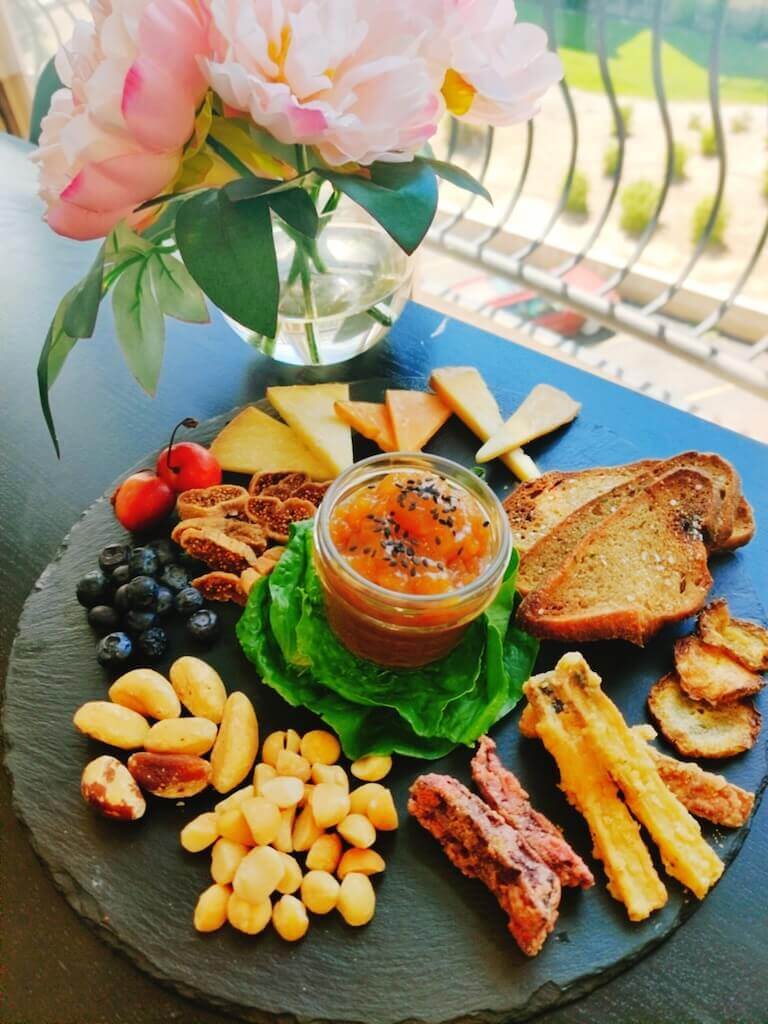A vegetarian charcuterie plate features blueberries, macadamia nuts, brazil nuts, tempura potato wedges, sliced figs, toast, fruit compote, and cheese.