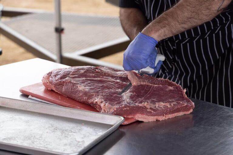 Chef prepping a cut of beef brisket by trimming fat from the meat.
