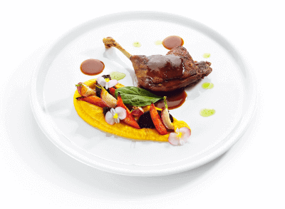 Fried duck leg with young vegetables, edible flowers, and carrot cream sauce on a white plate
