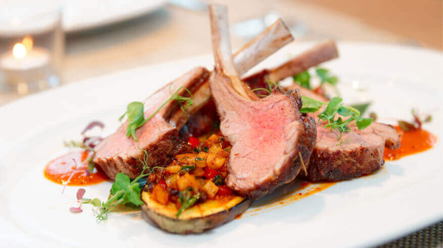 A gourmet restaurant plate of grilled rack of lamb chops with vegetables and mango salsa garnish